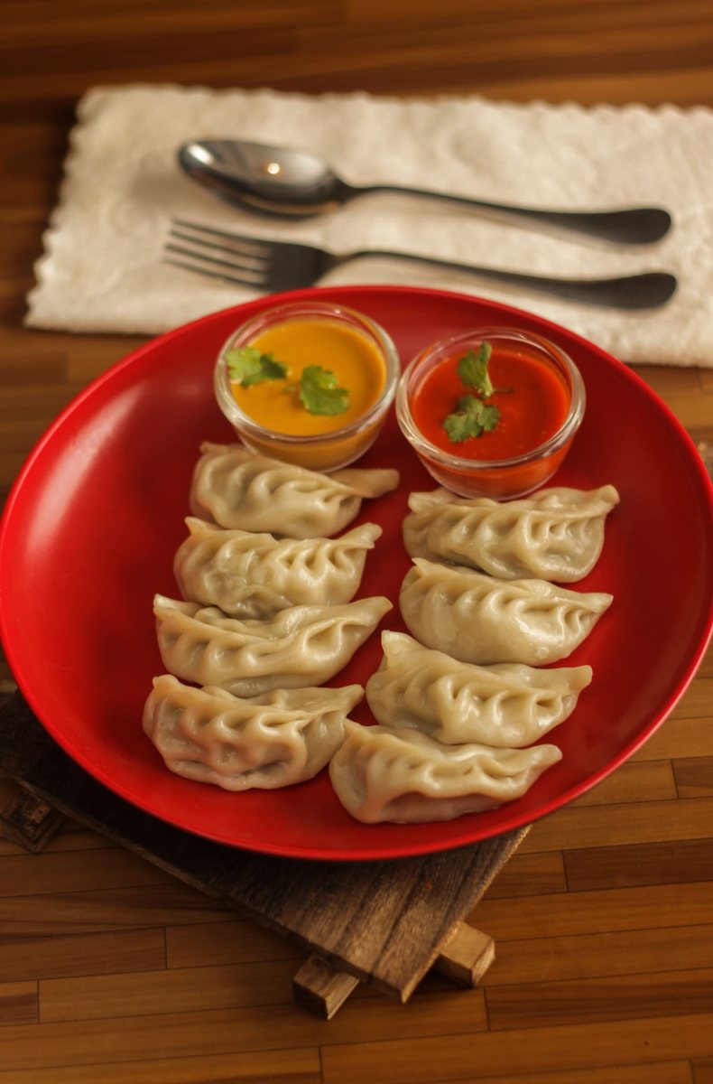 Steamed momos with two dipping sauces on a red plate
